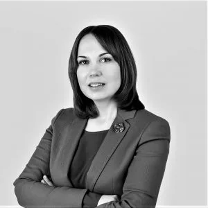 A professor with short dark hair is posing in a suit with her hands crossed on the chest.