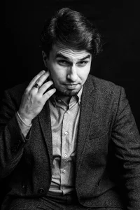 A professor with dark hair and a suit is posing for a picture.