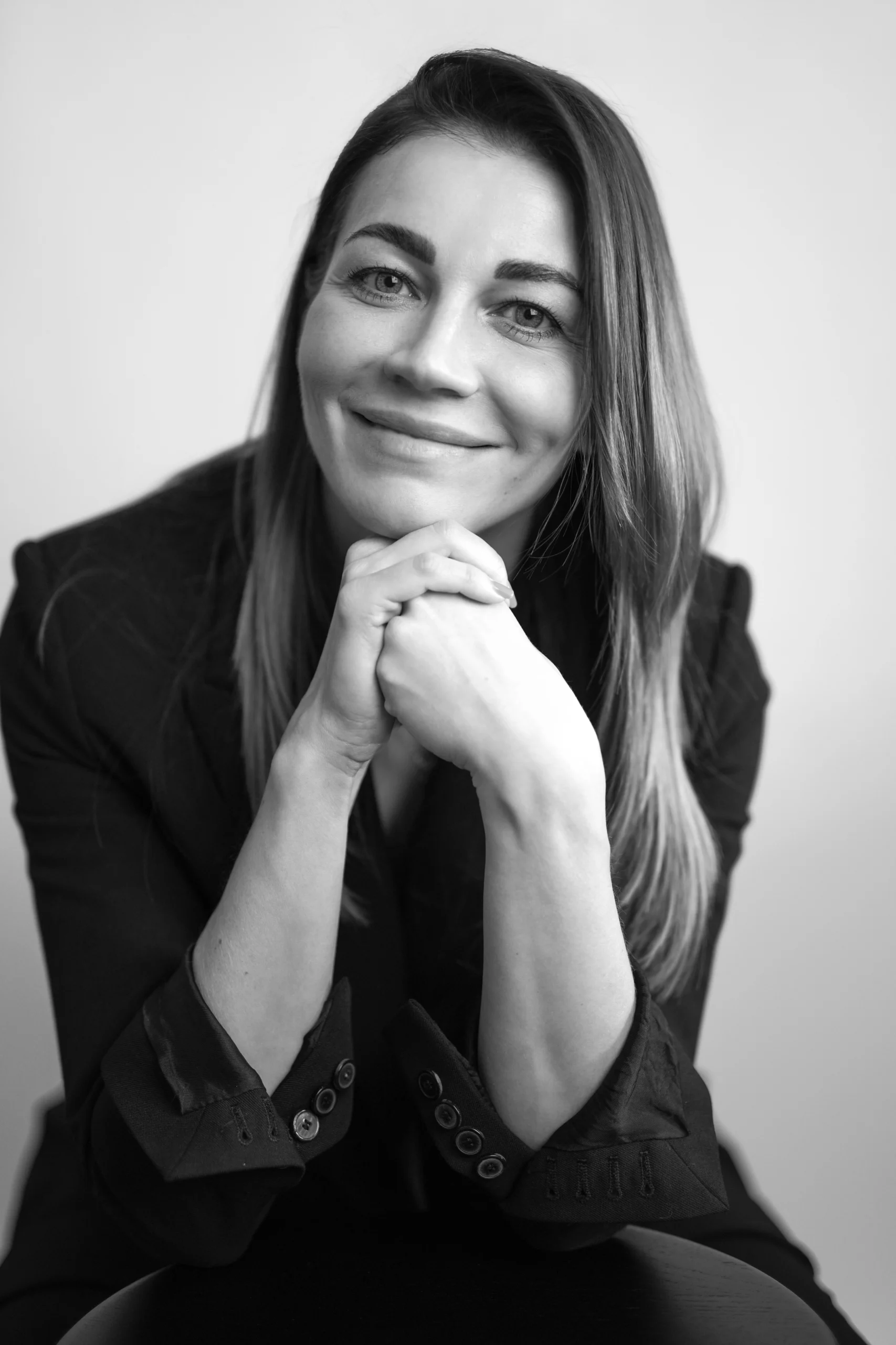 A happy professor is posing for a picture resting her chin on her clasped hands.