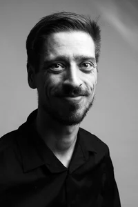 A happy professor with moustache, a beard and a black shirt is posing for a picture.