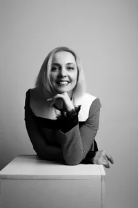 Happy professor with light, short-hair is posing for a picture while resting her chin on her hand.