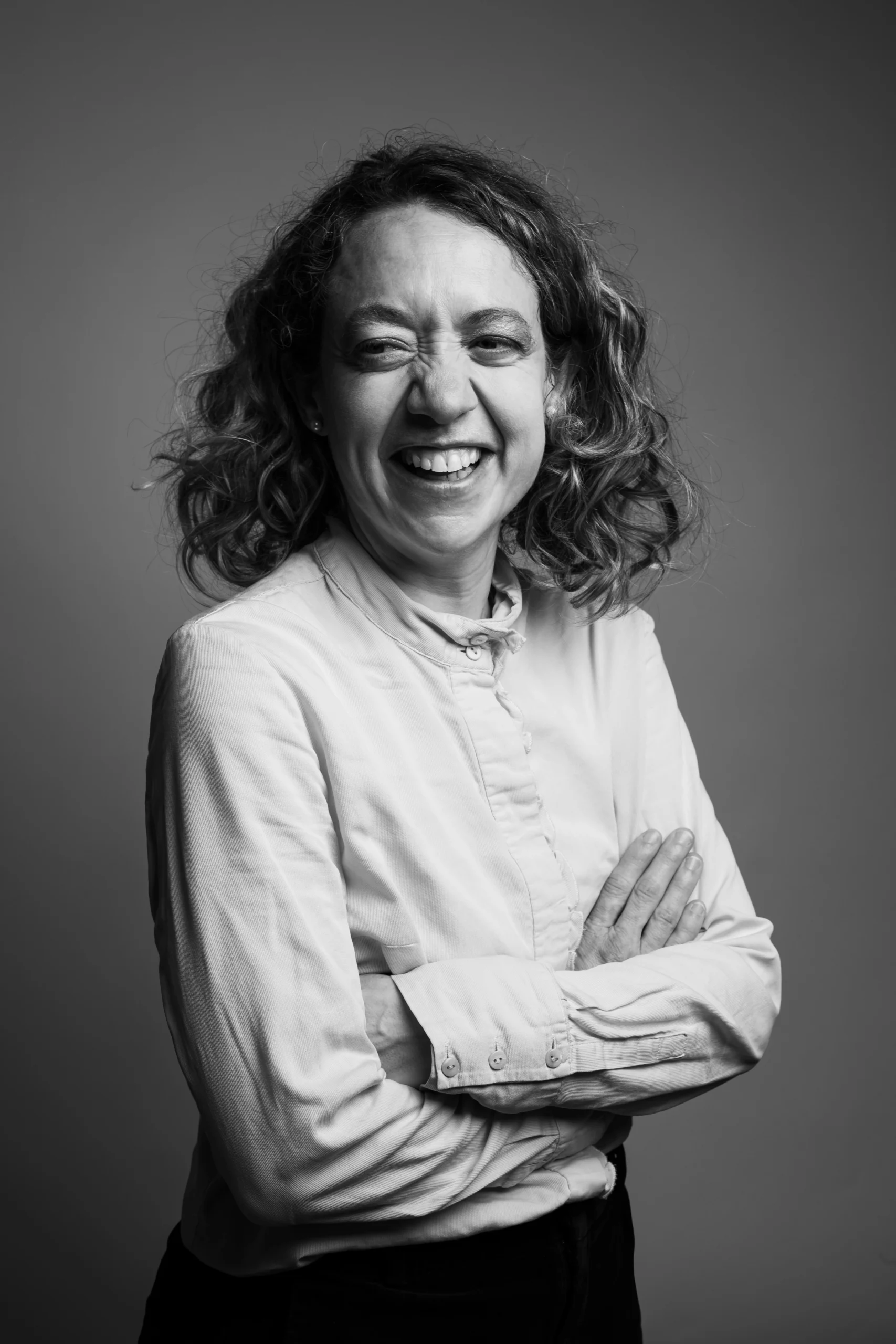 A happy professor is posing for a picture wearing a white button up with her hands crossed on her chest.