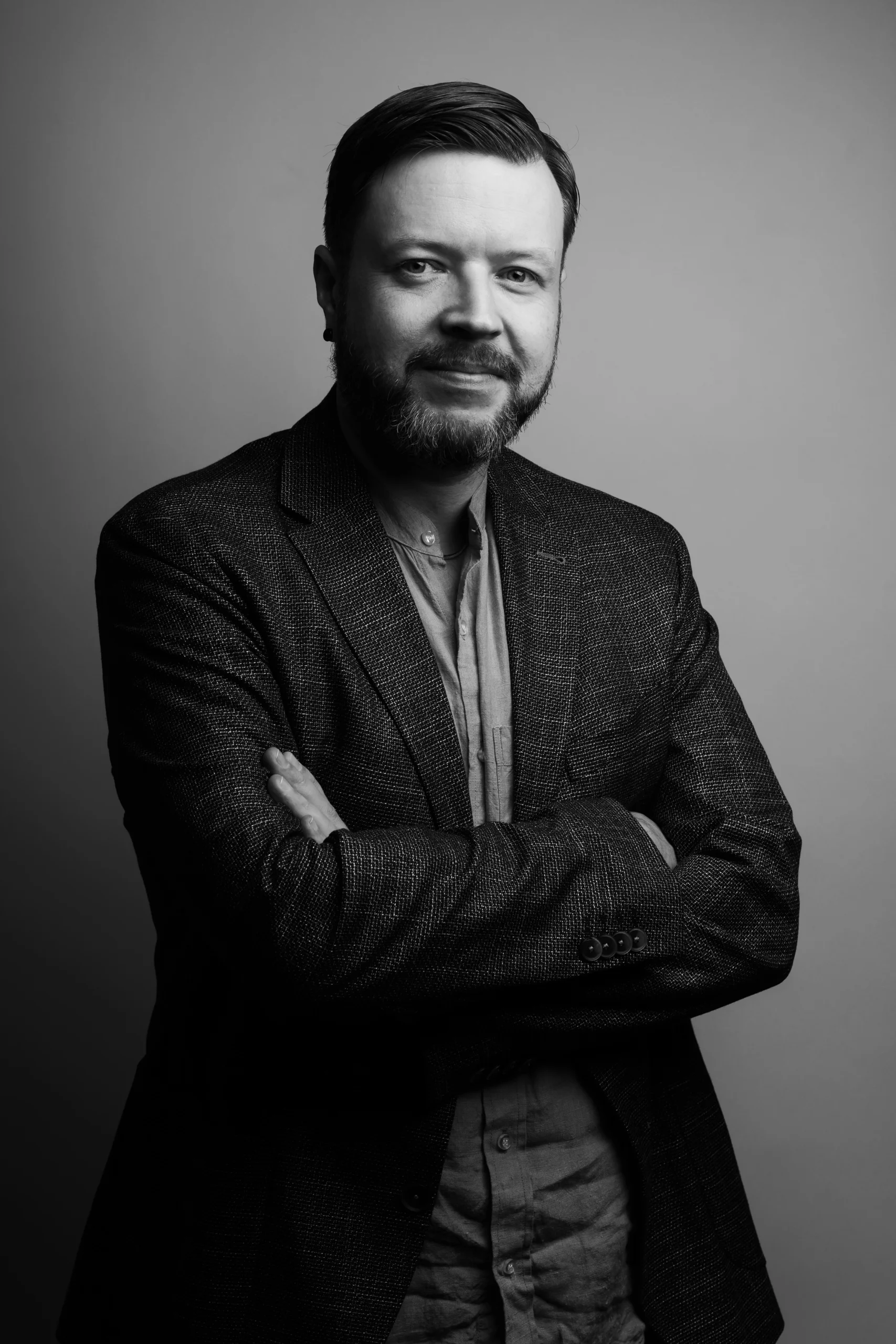 A professor in a suit is posing for a picture with his hands crossed on his chest.