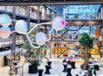 A contemporary collaboration space with industrial-style architecture, glass walls, and an artistic light installation, where people work and discuss in a creative, innovative environment.