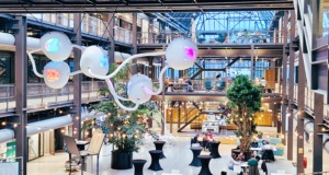 A contemporary collaboration space with industrial-style architecture, glass walls, and an artistic light installation, where people work and discuss in a creative, innovative environment.